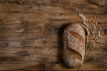 Bread with oat flakes and oat florets on old wooden background with space for text, top view.の写真素材