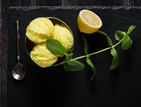 Top view of lemon sorbet ice cream, served with leaves of mint over black slate. Old  black wooden background.の写真素材