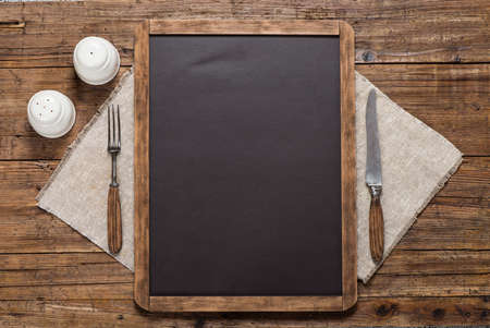 Blackboard for your text, spices, vintage spoon and fork on linen napkin on a rustic wooden table Top view with copy space.の写真素材