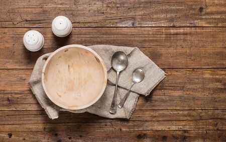 View from above of empty wooden bowl and vintage spoons and linen napkin on a old wooden table.の写真素材