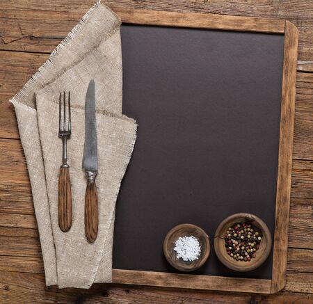 View from above of spices, vintage spoon and fork on linen napkin on a blackboard on a rustic wooden table with copy space.の写真素材