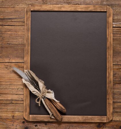 View from above of vintage spoon and fork tied with string on linen napkin on a blackboard on a rustic wooden table with copy space.の写真素材