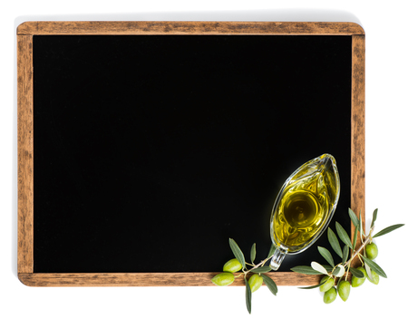 View from above of olive oil in a glass sauce boat and green olive fruits on a blackboard with copy space isolated on white background.の写真素材