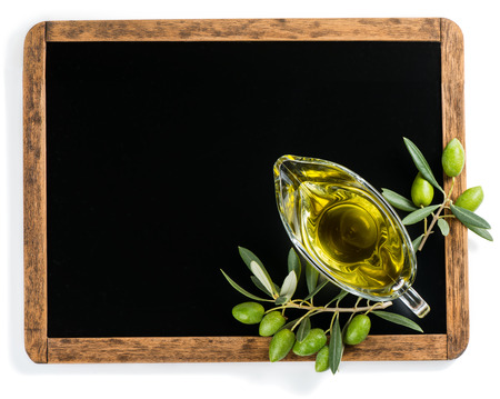 Top view of blank blackboard with olive oil in a glass sauce boat and green olive fruits over white background. Empty chalkboard for your text.の写真素材