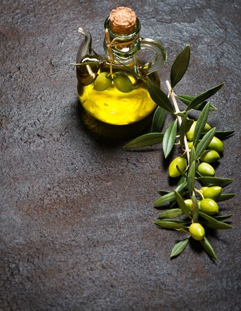 Branch with green olives and glass bottle olive oil on a black grunge metal background.の写真素材