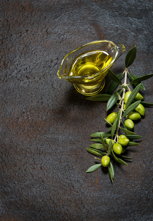 Branch with green olives and glass sauce boat of olive oil on a black grunge metal background.の写真素材