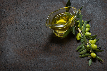 Twig with green olives and glass sauce boat of olive oil on a black old  metal background.の写真素材