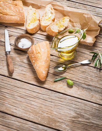 Slices of bread, salt, olives fruit with green leaves and bowl of olive oil  on a rustic wooden background with copy space.の写真素材