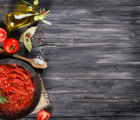 View from above of tomato sauce in a pan and ingredients (tomatoes, spices, olive oil) on a rustic black wooden table with copy space.の写真素材