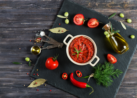 Top view of spicy tomato sauce in a white casserole and ingredients around (tomatoes, spices, olive oil) on a black slate board.の写真素材