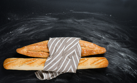 Top view of fresh baked traditional baguettes bread tied together with napkin on a floured black chalkboard with copy space.の写真素材