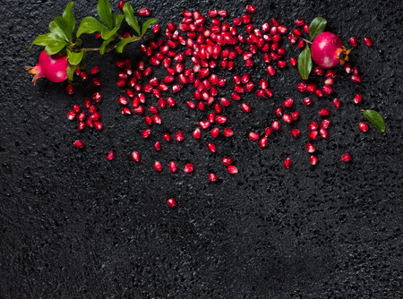Top view of loose pomegranate seeds and twigs of pomegranate tree with fruit and green leaves on a black background with copy space.の写真素材