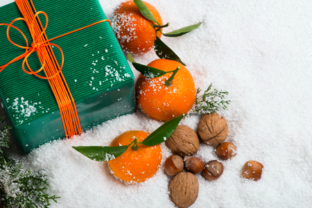 Top view of christmas  gift box, walnuts, hazelnuts, tangerines with green leaves on a snow background with copy space.の写真素材