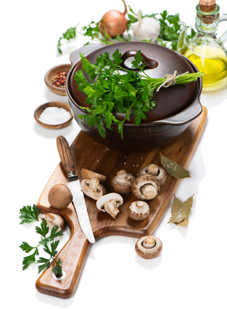 Cooking pot and uncooked ingredients for mushroom soup (fresh brown champignon mushrooms, olive oil, spices) on a cutting wooden board isolated on white background.の写真素材