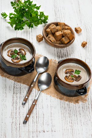 Two of portions of mushroom cream soup serving with croutons and parsley on a white rustic wooden table with copy space.の写真素材