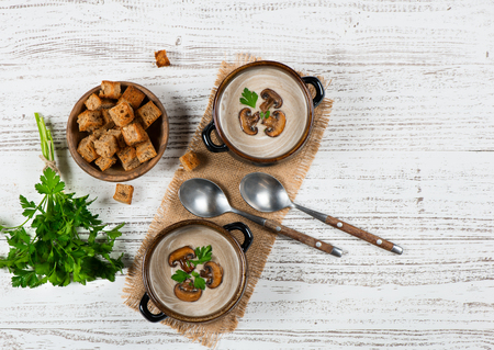 Top view of two bowls of portions of mushroom cream soup serving with croutons and parsley on a white rustic wooden table with copy space for text.の写真素材