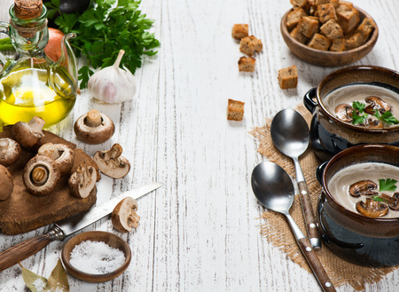 Mushroom cream soup and uncooked ingredients  (fresh brown champignon mushrooms, olive oil, parsley, spices), croutons on a white rustic wooden table with copy space for text.の写真素材