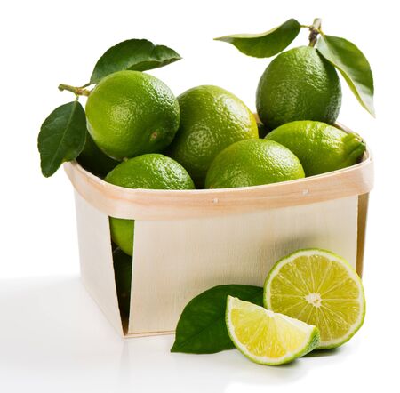 Lime fruits with green leaves in a crate with cuted one on the surface in the foreground isolated on white background.の写真素材