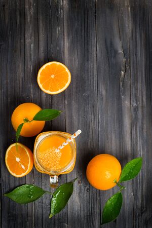  Top view of freshly squeezed orange juice in a mason jar and fresh oranges fruits with green wet leaves on a wooden rustic table with copy space.の写真素材