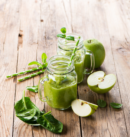 Vegetable and fruit smoothie and ingredients ( apple and spinach) in mason jars on a rustic wooden background with copy space.の写真素材