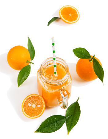 Freshly squeezed orange juice in a mason jar and orange fruits with green leaves isolated on white background.の写真素材