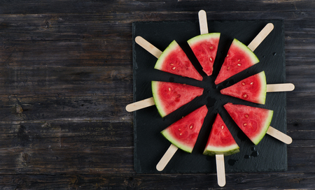 Watermelon slices on a sticks in a circle on wooden background with space for text. Top view.の写真素材