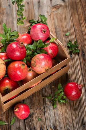Organic pomegranate fruits with green leaves in a box on rustic wooden table.の写真素材