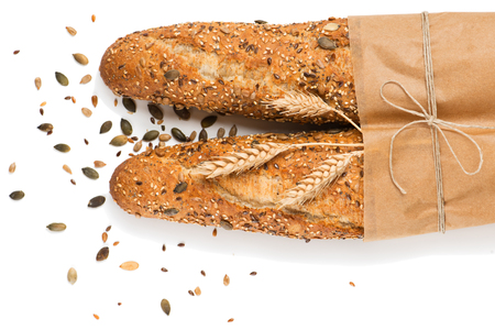 Top view of two baguettes baked bread in paper with different seeds ( pumpkin, poppy, flax, sunflower, sesame, millet ) decorated with ears of wheat isolated on white background.の写真素材