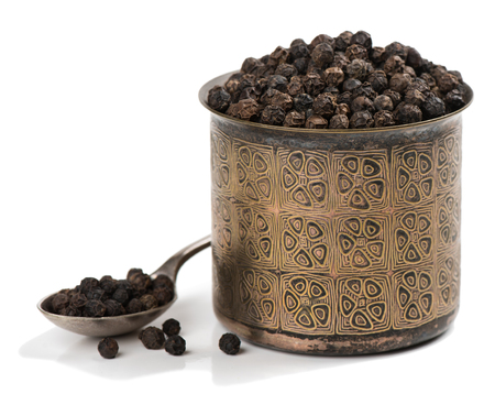 Black peppercorns in a bronze bowl and in the spoon isolated white background.の写真素材