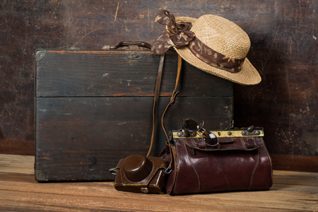  Old wooden suitcase, women's straw hat, retro camera and travel bag on a dark grunge background. The concept of travel.の写真素材