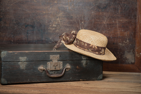 Women's wicker hat and retro suitcase on a dark wooden grunge background with copy space.  Retro style image.の写真素材