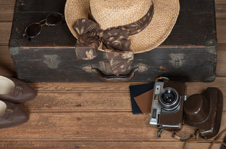  
Travel preparations: women's wicker hat, sunglasses, shoes, retro camera and old suitcase on a dark wooden grunge background with copy space.  Retro style image.の写真素材