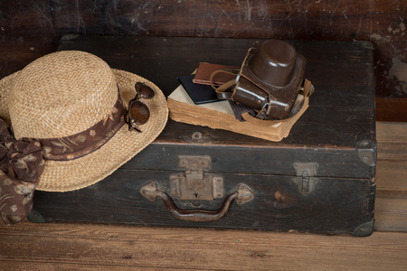 Travel concept with vintage suitcase, wicker hat and old camera and book a dark wooden grunge backgroundの写真素材