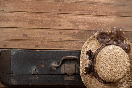 Top view of women's wicker hat, sunglasses and vintage suitcase on wooden floor with copy space.  Travel concept.の写真素材