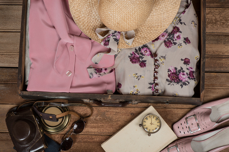 Vintage suitcase with women's clothes and accessories for summer travel: hat, camera, step-ins, sunglasses, clock and book on a  old wooden floor.の写真素材