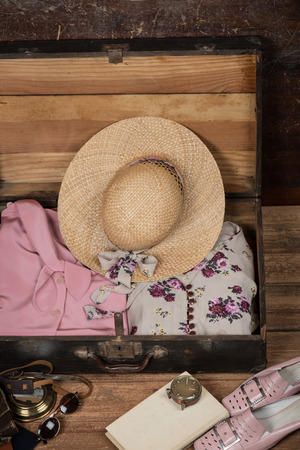 Ready vacation suitcase with women's clothes and accessories for summer travel: hat, camera, step-ins, sunglasses, clock and book on a wooden grunge background with copy space. The concept of travel.の写真素材