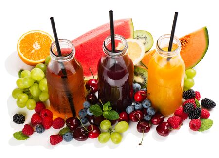 Three different glass bottles juice with many fresh summer berries and fruits isolated on whiteの写真素材