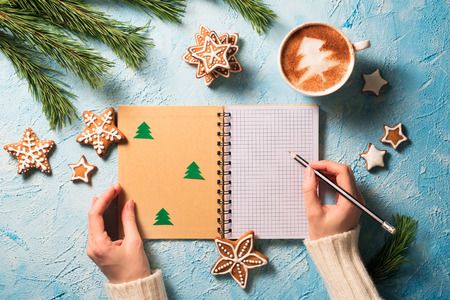 Christmas concept. Womans hands with peper note and cup of coffee with fir decorations over blue texture. Top view. Copy spase.の写真素材