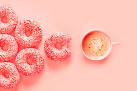 Donuts and cup of coffee in color of panton living coral, pink background, top view, flay lay