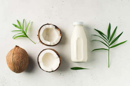 Coconut milk in glass bottle with coconuts on white background, vegetarian dairy eta, copy space, top view, flat layの写真素材