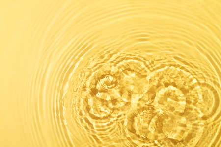 Transparent and clean yellow water background with sunlight reflection, top viewの写真素材