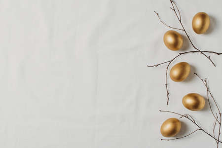 Easter concept with golden eggs and twigs flat lay on white texture background, copy space, top viewの写真素材