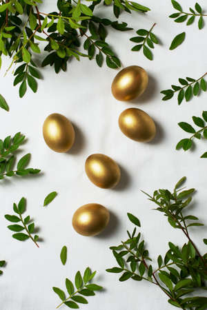 Easter concept with gold eggs and branch with green leaf on white background, top view, copy space, flat lay, verticalの写真素材