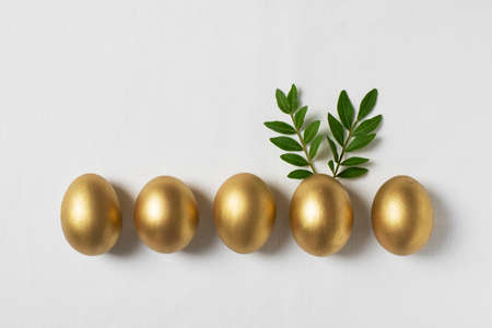 Easter concept with gold eggs and branch with green leaf on white backgroundの写真素材