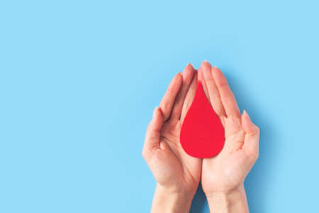 World hemophilia day concept with red blood drop simbol and hands on blue backgroundの写真素材