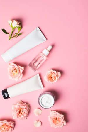 Bottles of serum and cream tube with rose flowers flat lay on pink background, copy space, top view, verticalの写真素材