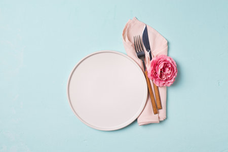 Tableware setting with fork, knife, napkin and flower on blue background, spring serving, top view, copy space, flat layの写真素材