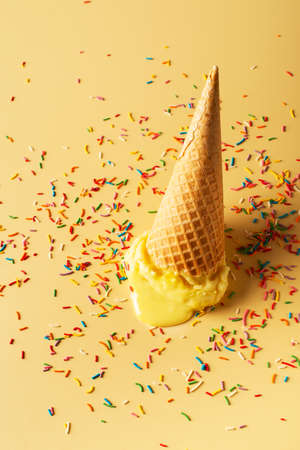 Melted yellow ice cream cone with confetti creative pastel background, copy space, veticalの写真素材