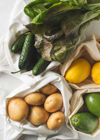 Zero waste concept. Textile ecologiical shopping bags with fruits and vegetables on white...