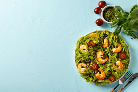 Green pasta with shrimp, basil and tomato on blue background, top view, copy space, flat layの写真素材